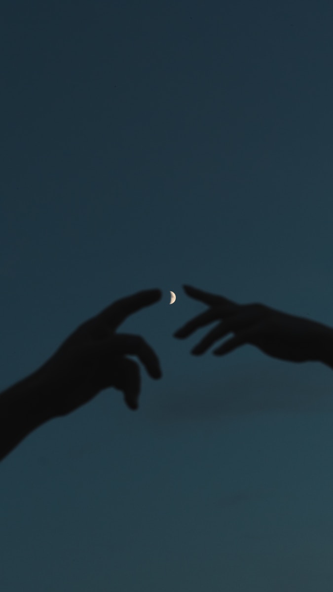two hands reaching for the moon in the sky